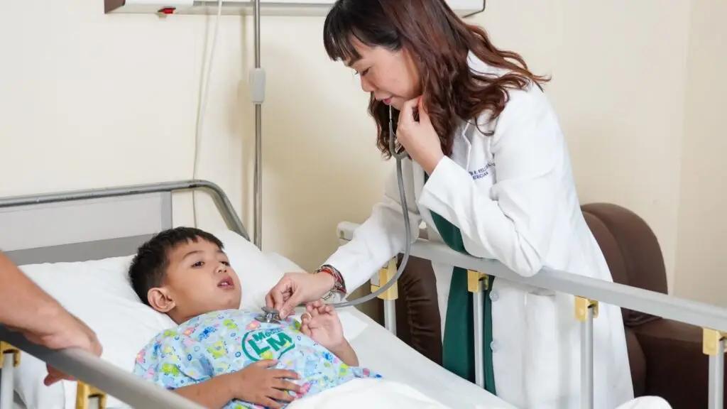 Doctor using stethoscope to examine child in hospital bed.